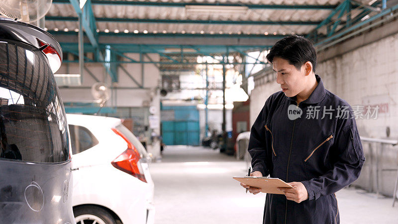 亚洲保险从业人员身穿技工服手持文件检查发生事故的汽车状况准备估算修理汽车的费用。