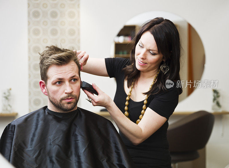 一个黑发女人在理发店给一个男人剪头发