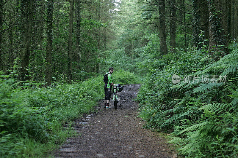 年轻的成年男子骑着山地车在森林小径上