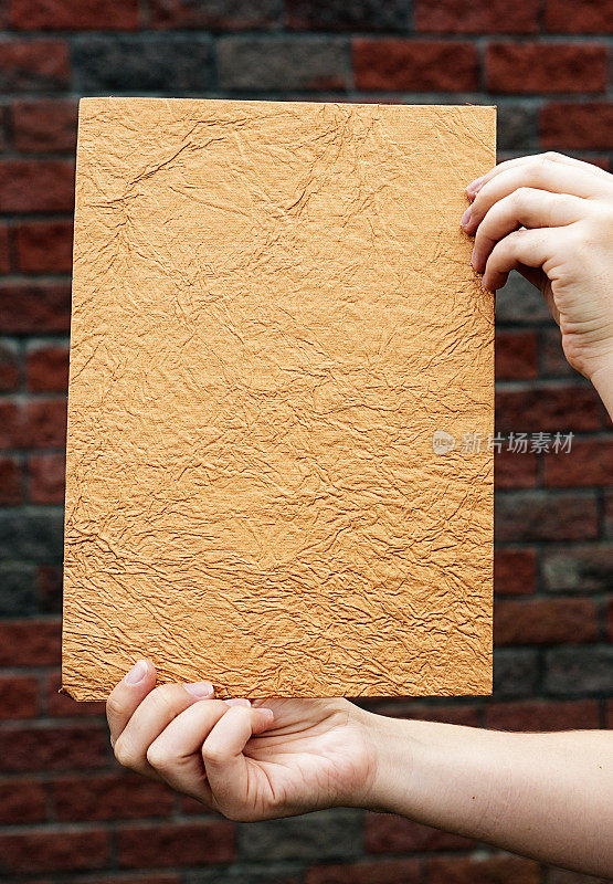 女性手里拿着一张棕色的、有纹理的纸贴着砖