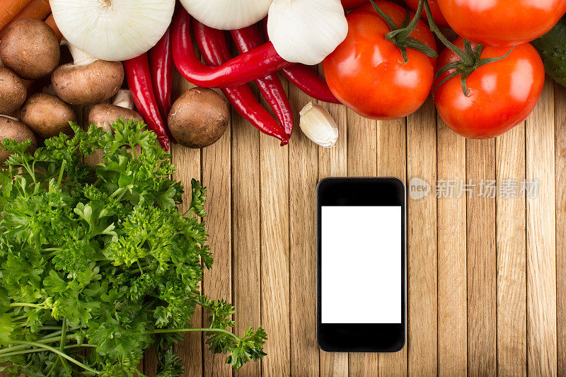 木桌上放着一部空白的智能手机，周围都是蔬菜