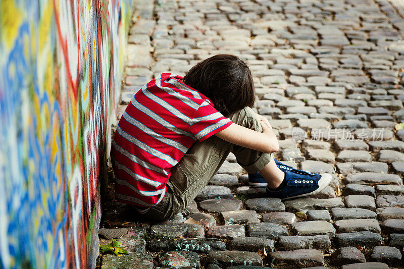 一个小男孩坐在墙上，头靠在壁画上