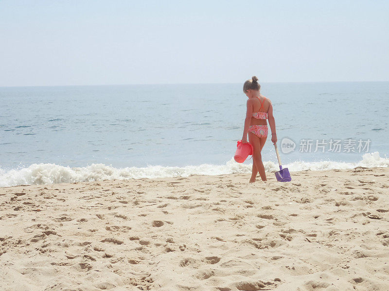 沙滩上拿着桶和铲子的女孩