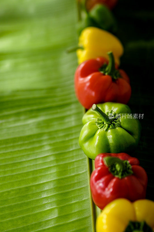 把新鲜的红、绿、黄辣椒或甜椒放在桌上的香蕉叶上。