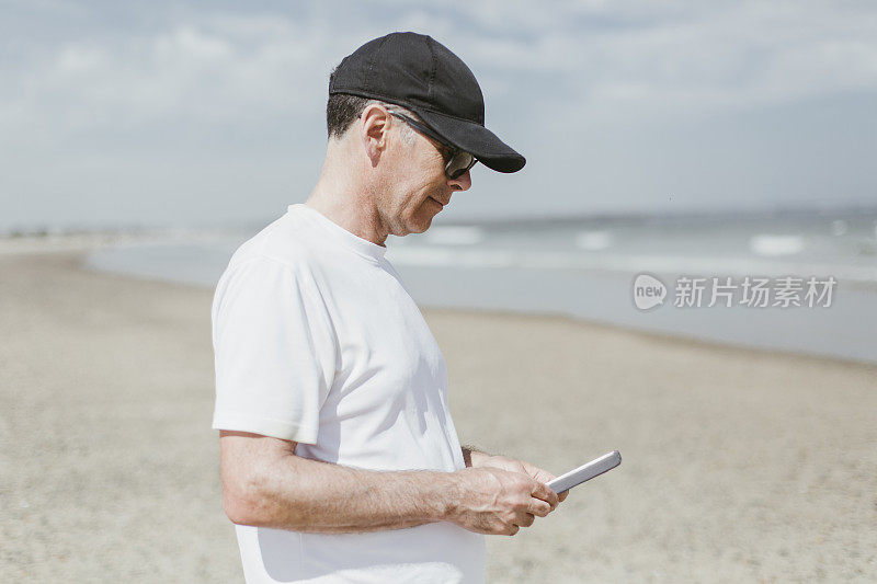 一个在海滩上看手机的成熟男人的肖像