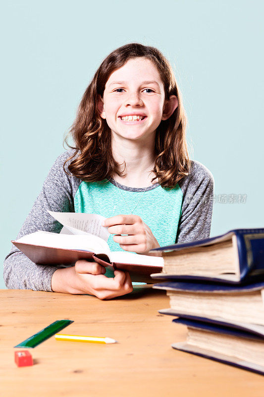 可爱的，微笑的十多岁的女孩从她正在阅读的书抬起头