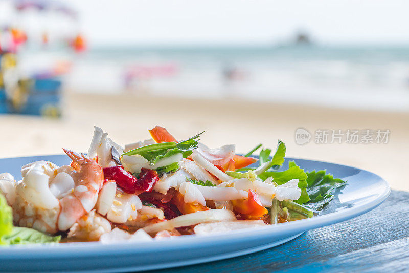 辛辣海鲜沙拉是一种泰式健康食物，它将粉丝、鱿鱼、虾、洋葱、辣椒和香草混合在泰国街头小吃的木桌上