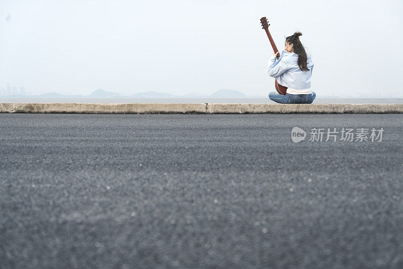 年轻女子坐在河边弹吉他