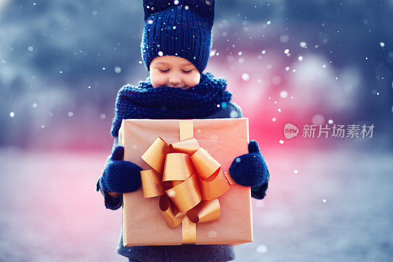 可爱的孩子在大雪下拿着大礼盒。专注于礼品盒