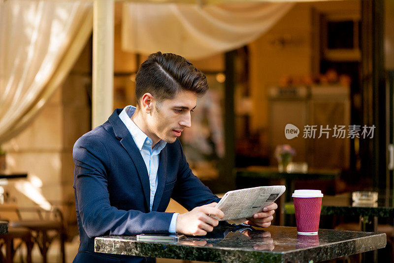 年轻男子穿着西装在外面看报纸喝咖啡