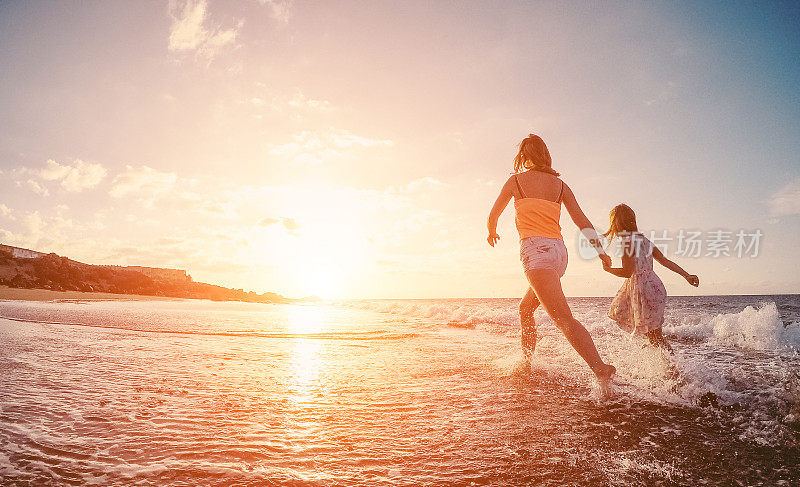 妈妈和女儿在热带海滩的水里跑步-妈妈和她的孩子在海边度假-家庭生活方式和爱的概念-关注身体轮廓