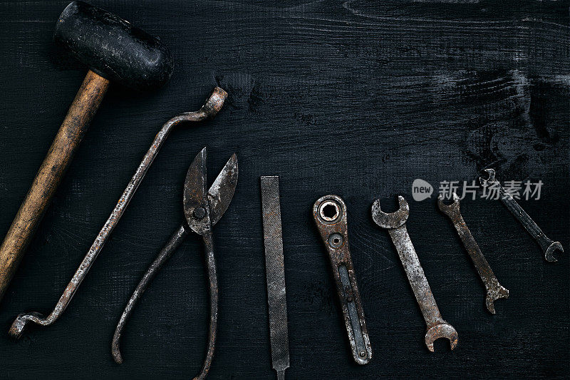 旧的生锈的工具放在一张黑色的木桌上。锤子，凿子，金属剪刀，扳手