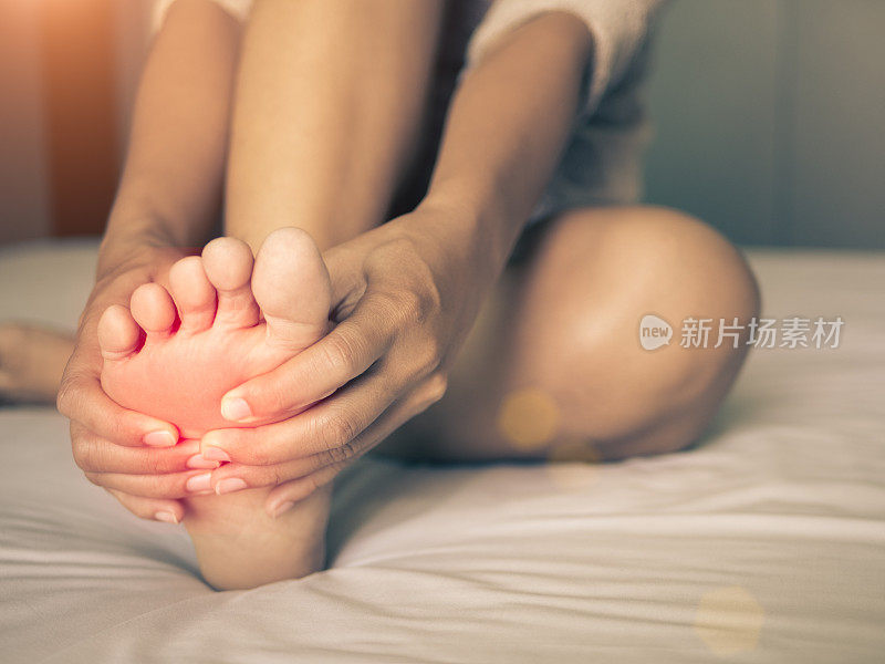 卫生保健的概念。一个女人在按摩她疼痛的脚，疼痛部位的红色高光