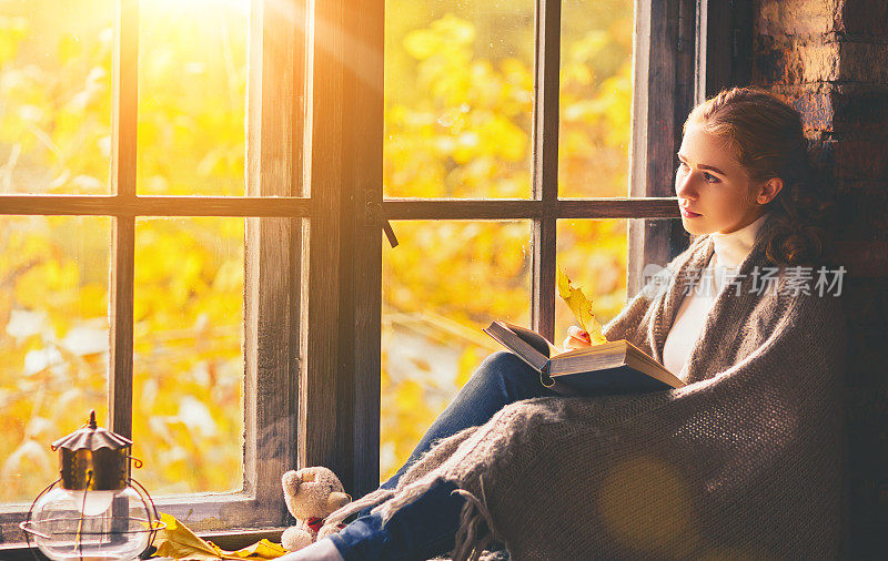 快乐的女人在秋天的窗边看书