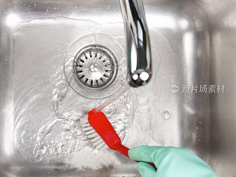 手持橡胶手套的手拿着红色的刷子擦洗水槽