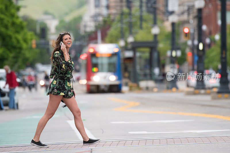 一名年轻女子在美国斑马线上过马路时，正在打手机，背景是有轨电车