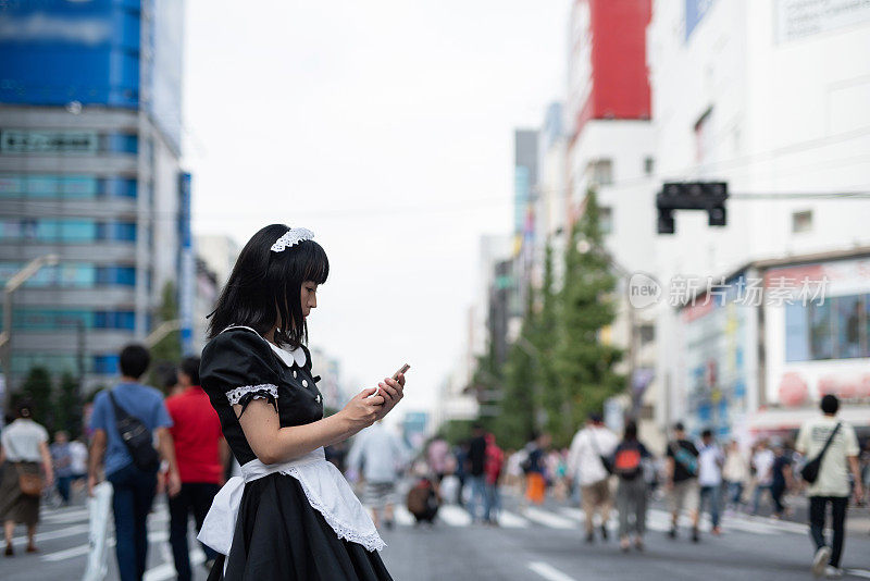 在东京秋叶原街头，Cosplay女仆在看智能手机