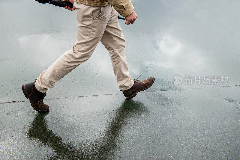 一名男子撑着伞在潮湿的柏油路上行走