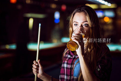 一个女人在打台球的时候喝着一杯啤酒