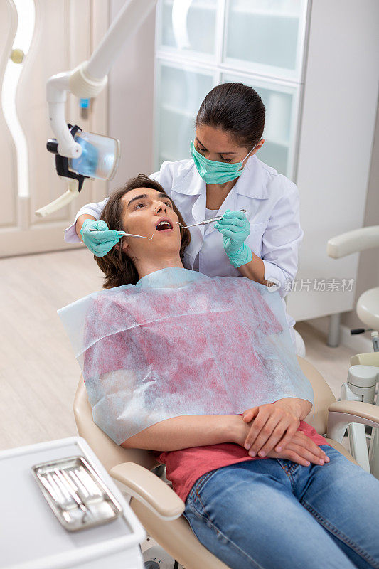 牙医拿着牙科工具在一个年轻的病人身上