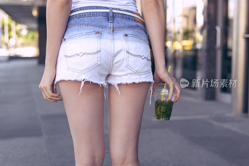 裁剪近距离的照片，女士的背部穿白色牛仔蓝色迷你短裤合身的瘦腿拿着塑料杯在手里