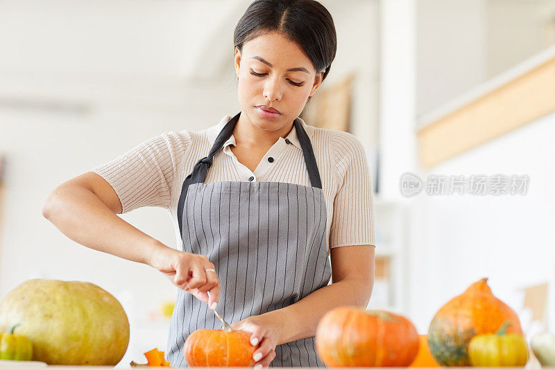 穿着围裙的年轻黑人妇女在家里做南瓜灯的时候从南瓜里取出种子