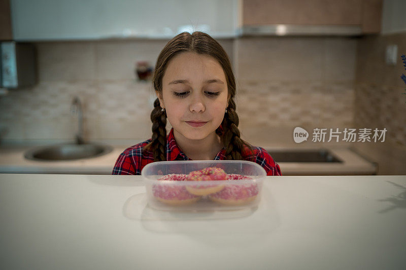 对孩子的饮食。悲伤和不快乐的孩子触及甜甜圈。孩子们的美味食物。孩子在看甜甜圈。垃圾食品上瘾。