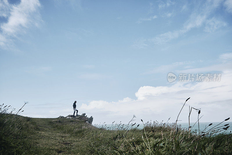 一名男子站在悬崖上，在纽基看康沃尔海岸线的景色。