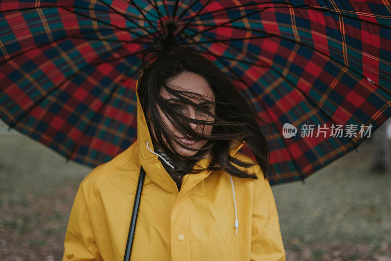 穿着黄色雨衣的年轻女子在公园里度过雨天