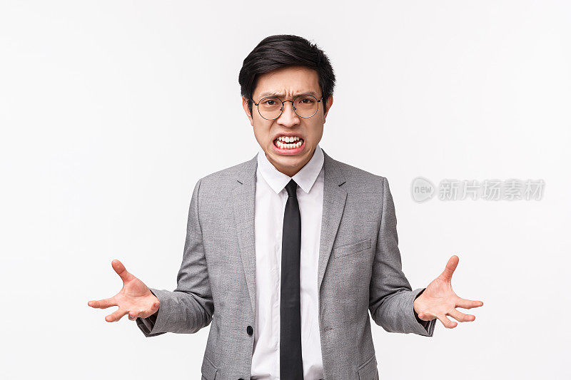 这是一幅愤怒愤怒的年轻亚洲男性办公室职员的肖像，他们感到攻击性和紧张，失去耐心，因为憎恨和愤怒而握紧拳头，因为烦恼而做鬼脸，因为愤怒而沸腾
