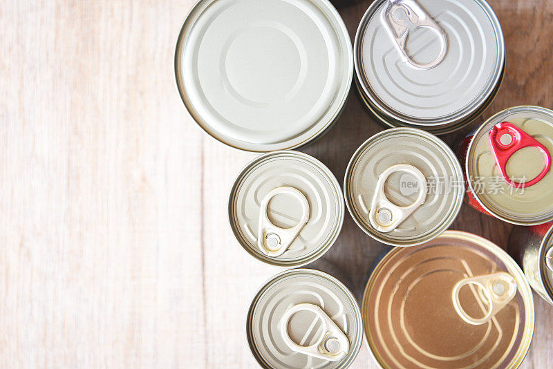 各种罐头食品在金属罐头木质的背景下，俯视图罐头食品不易腐坏的食品储存在厨房的物品或家庭或捐赠