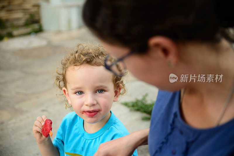 蹒跚学步的孩子拿着西瓜冰棒，嘴巴凌乱地看着相机