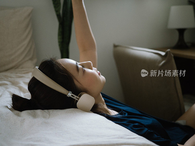千禧亚洲女性戴着耳机在家听音乐