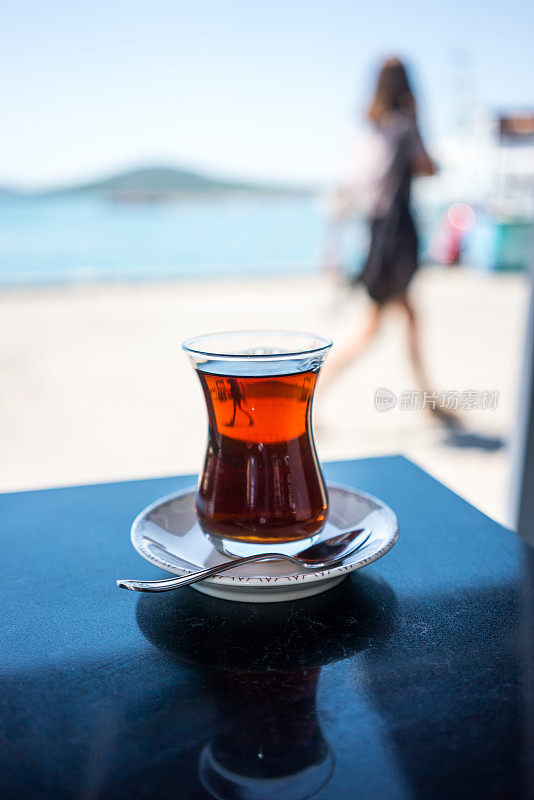 海边桌子上的土耳其茶杯里盛着红茶，一个女孩正在走