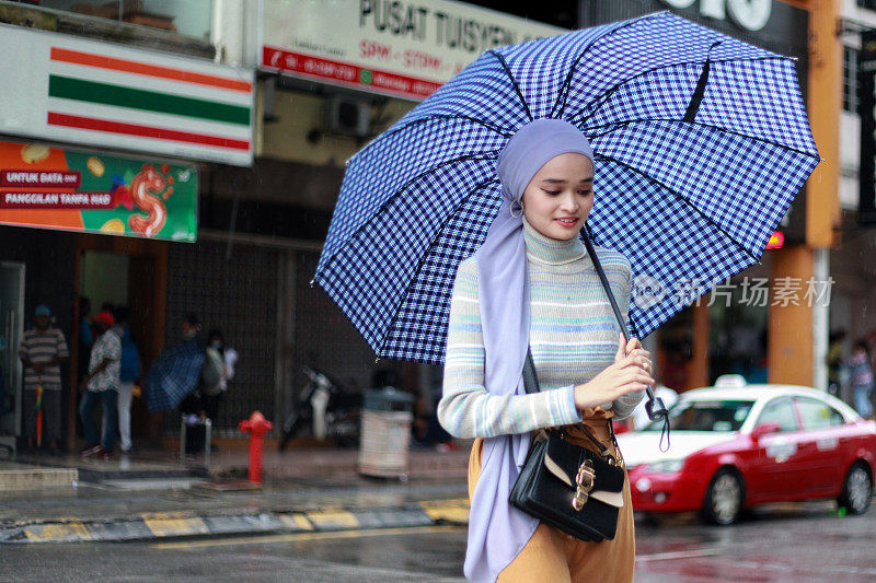 一位戴着头巾、撑着伞的穆斯林马来妇女在雨中行走