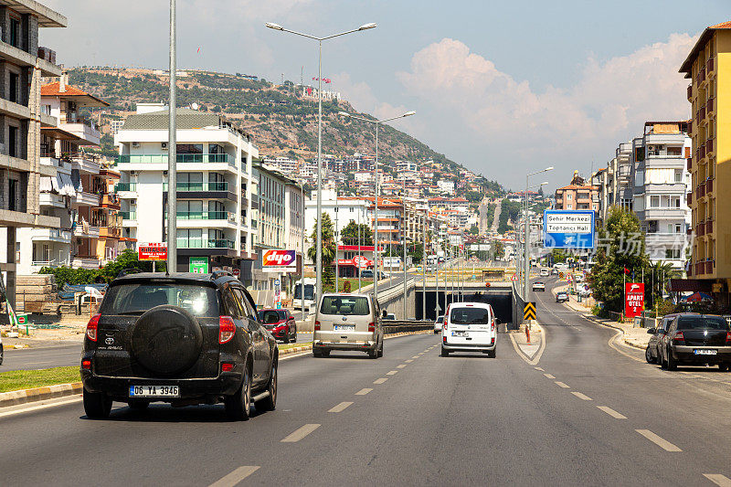 驾驶在土耳其的概念。汽车在交通拥堵的安塔利亚-梅尔辛高速公路中间带着风景秀丽的风景进入山上，山上挂着“我爱阿兰亚”的标牌。