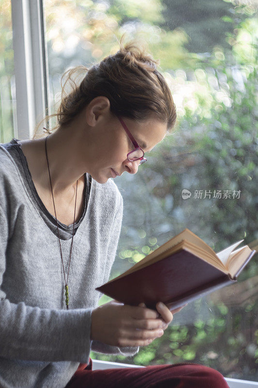 戴眼镜的女人在窗前看书