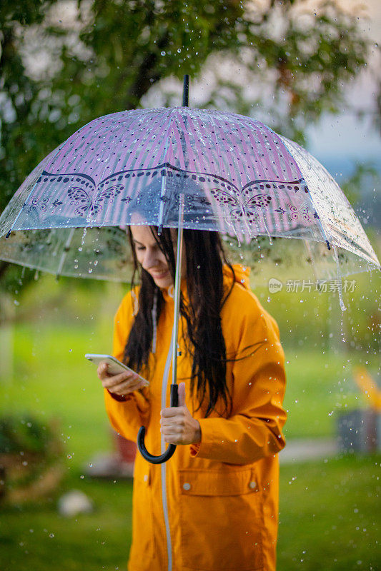 一个年轻的女人在雨中穿着黄色雨衣使用手机的肖像