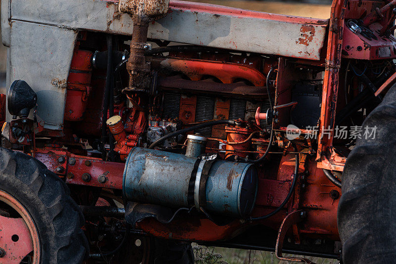 在阳光明媚的秋日保加利亚农村，旧的银色柴油坦克上红色的老式俄罗斯拖拉机发动机可见电线生锈和油滴