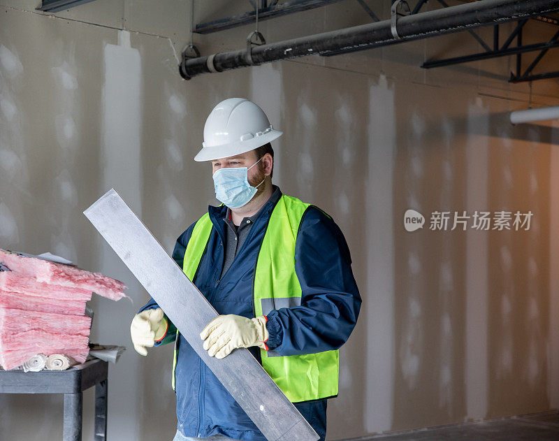 建筑工人或工程师在工地上搬运材料并查看剪贴板上的平面图