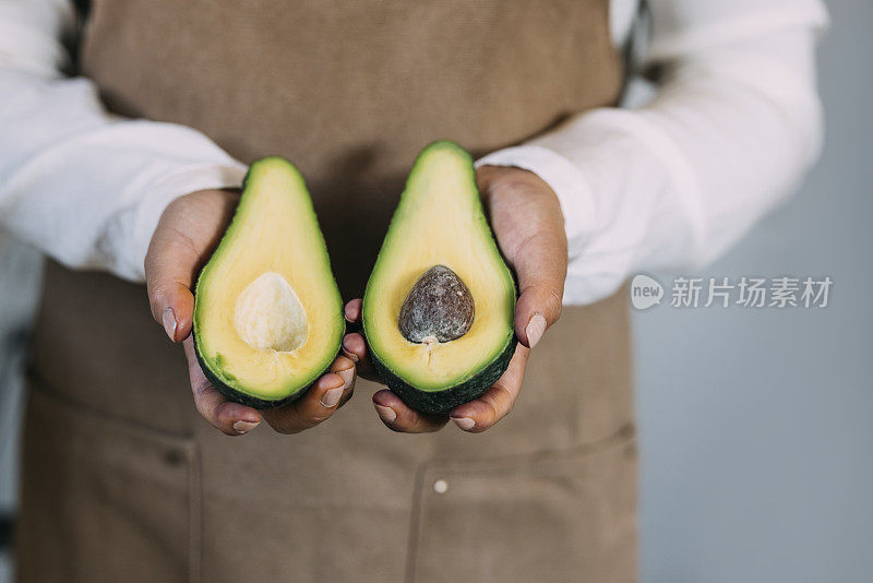 近距离拍摄的匿名女人的手拿着一个打开的鳄梨水果