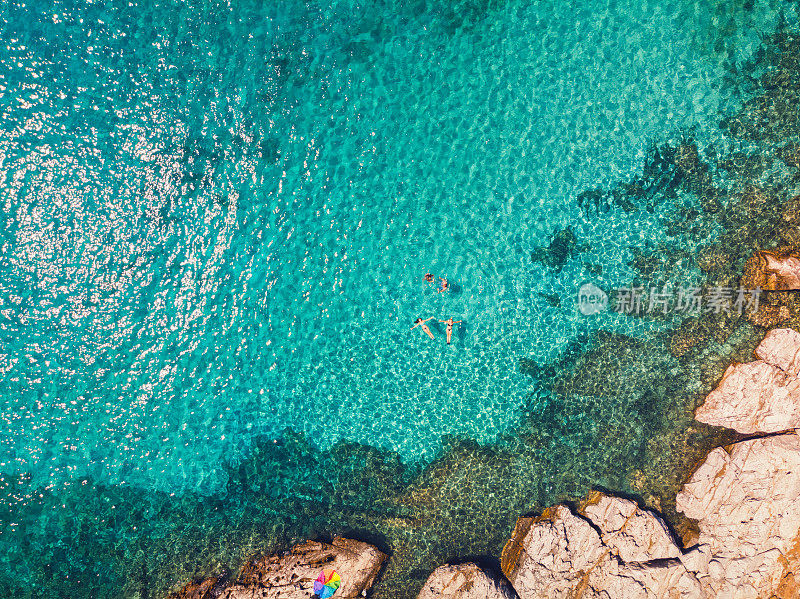 鸟瞰图一个年轻的家庭漂浮和游泳在美丽的海滩在希腊岛