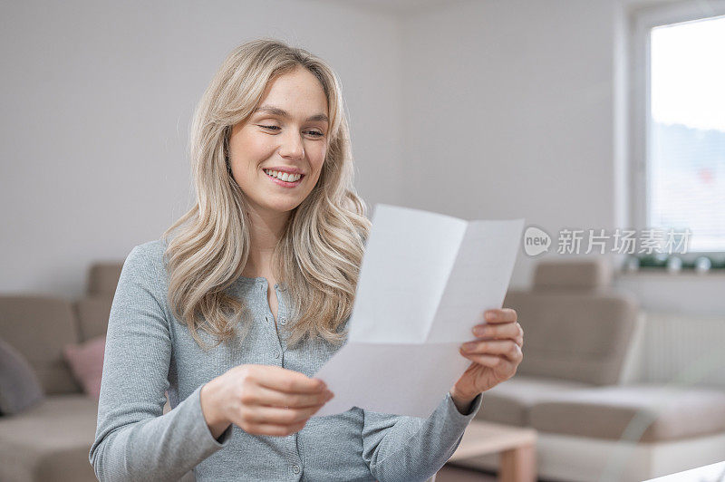 年轻女子微笑着在家里读一封信