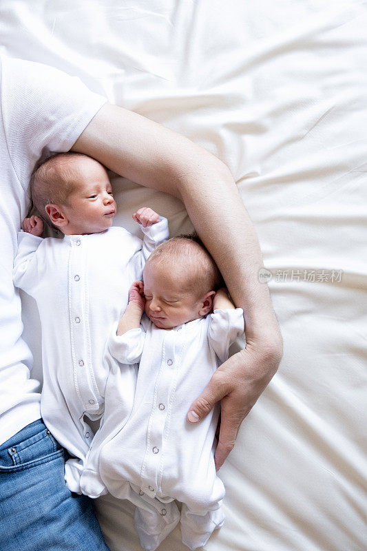 刚出生的同卵双胞胎在床上，在父母的手上。生活方式，孩子的情感。婴儿婴儿与复制空间