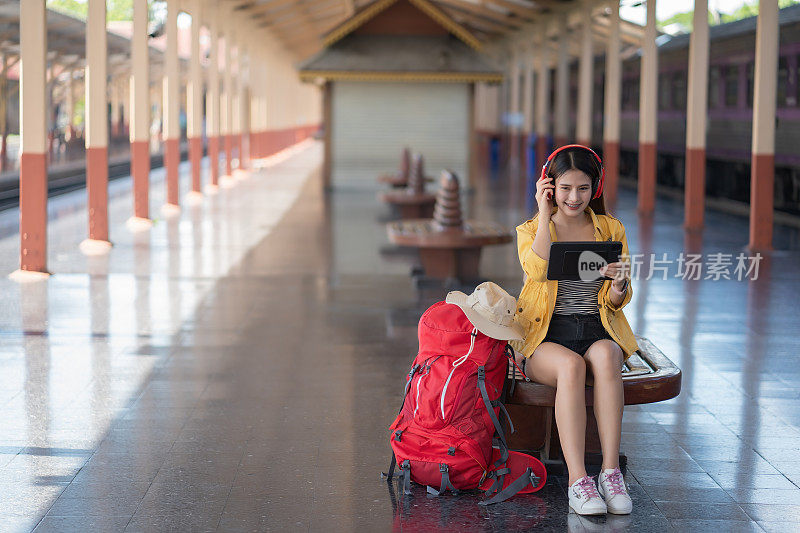 一个年轻的旅行者戴着耳机，在火车站的月台上用平板电脑寻找一个地方。