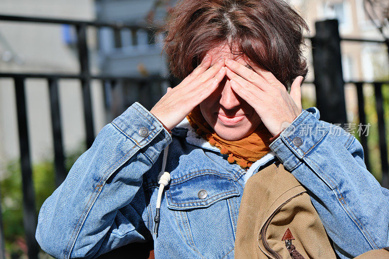 在秋天的城市街道上，一个成熟的女人正在用手闭上眼睛