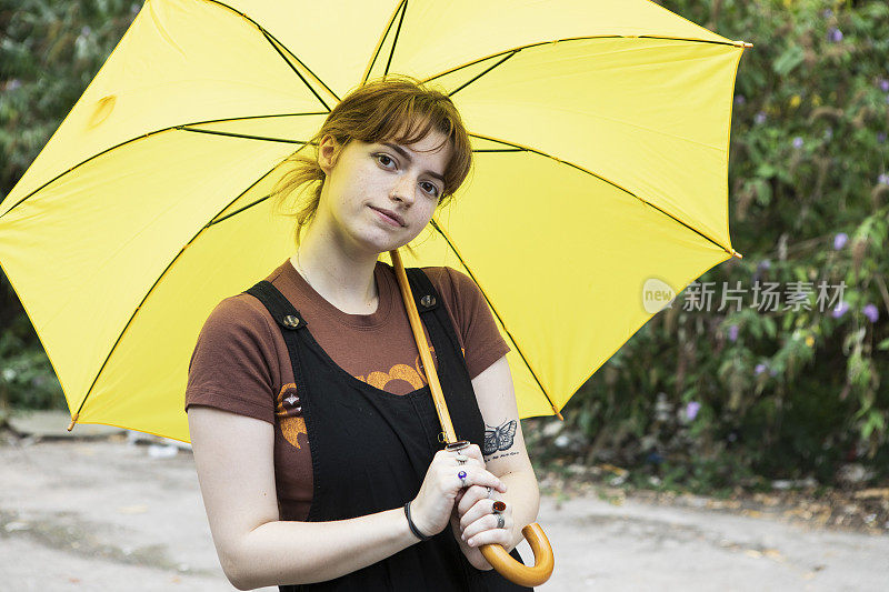 一个年轻的女人拿着一把黄色的伞，看着镜头