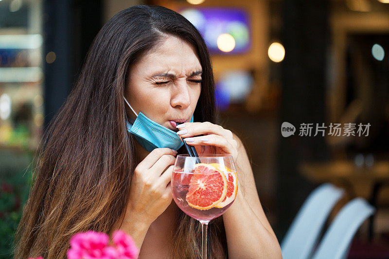 年轻女子戴着防护口罩喝着鸡尾酒