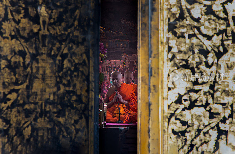 透过半开的门，佛家的和尚们坐在主维汉殿里祈祷并敬拜佛像。