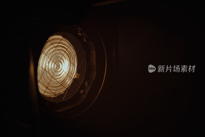 在黑暗的背景上，使用菲涅耳镜头的专业照明设备的特写。照片中的照明装置在左上方，在右下方发光。